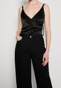 Svart satin wrap-top med tunna axelband, kombinerad med högmidjade svarta denimbyxor med prickiga dekorationer och sidofickor.