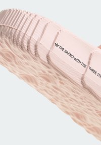 Sportssko med en texturerad rosa sula som har ränder och spår. Inkluderar varumärkestext i svart nära toppen och en slät yta.