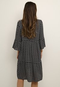 Vestido de patrones en blanco y negro con mangas de campana de tres cuartos, diseño en capas y tejido ligero. Presenta formas geométricas en toda su superficie.