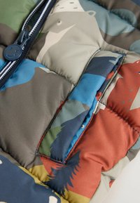Quilted puffer jacket in multicolored camo pattern featuring a blue zipper, pocket, and a mix of green, brown, and orange tones.