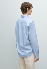 Světle modrá košile s dlouhými rukávy a límečkem, vyrobená z bavlny, s sklady na zadní straně pro dodatečný detail a strukturu.