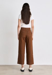 Pantalons larges marron à taille haute, en denim, avec des poches arrière visibles et un ourlet net, associés à un t-shirt blanc uni.