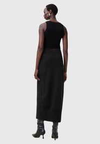 Zwart mouwloos topje, gecombineerd met een lange zwarte gebreide rok. De outfit heeft een rechte silhouet en wordt aangevuld met zwarte haklaarzen.