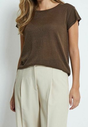 Femme portant un haut en maille marron à manches courtes rentré dans un pantalon plissé taille haute beige clair sur un fond uni.