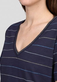 T-shirt bleu marine avec un col en V, des manches courtes et des rayures horizontales en bleu clair et or. Tissu doux avec une texture subtile.