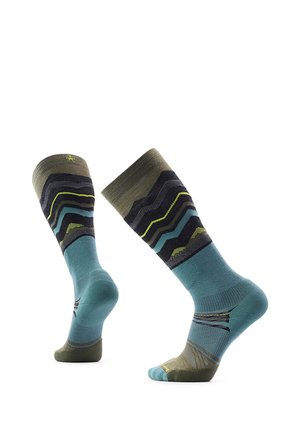 Par de calcetines hasta la rodilla con patrones en zigzag azul, verde oliva, negro y amarillo sobre un fondo blanco.