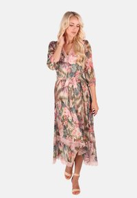 Blumenkleid in leichtem, transparentem Stoff mit tailliertem Gürtel. Mit rosa Spitzenbesatz und V-Ausschnitt. Der Hintergrund ist weiß.