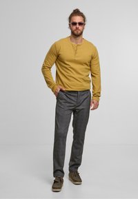 Mustard long-sleeve henley shirt with three buttons, paired with gray textured trousers and brown lace-up shoes.