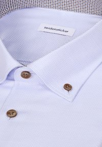 Col de chemise blanche texturée avec trois boutons marron et étiquette de marque "seidensticker" à l’intérieur.
