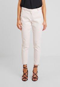 Pantalons ajustés rose clair avec un motif texturé, au design slim et longueur cheville, associés à des sandales noires à talons hauts et à lanières.