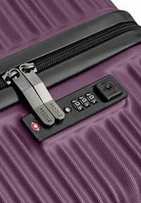 Maleta rígida morada con cremallera negra y candado de combinación TSA incorporado, mostrando los diales ajustados a 0-0-0 y tiradores de cremallera de metal dual.