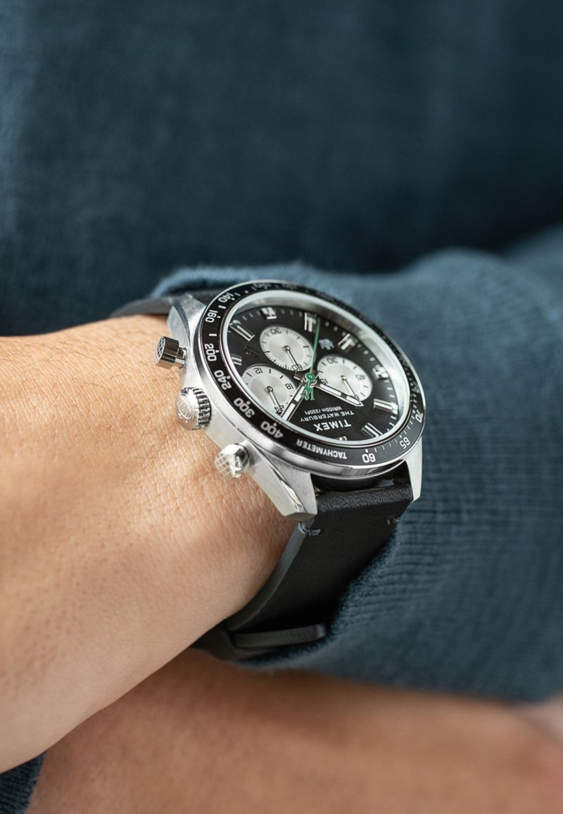 Schwarze Chronographuhr mit silbernen Akzenten, Gehäuse aus Edelstahl, schwarzem Gummiband, weißen Subdials und einer tachymetrischen Skalenlünette.