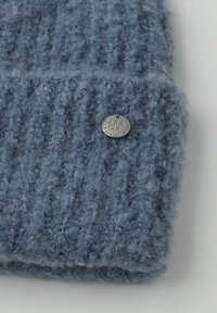 Gorro tejido azul suave con un patrón texturizado y una etiqueta circular plateada grabada con "Safa Street One".