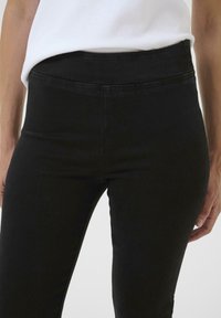 Schwarze hochtaillierte Jeans mit glatter Textur und elastischem Bund. Hat eng anliegende Beine und minimale Nähdetails.