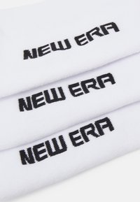 Calcetines tobilleros blancos con el texto negro "NEW ERA" bordado en múltiples capas. Tejido suave con una textura lisa y un diseño minimalista.