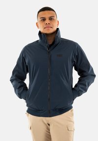 Chaqueta azul marino con cremallera hecha de un material ligero y suave. Cuenta con un cuello alto, puños elásticos y un logo en el pecho.