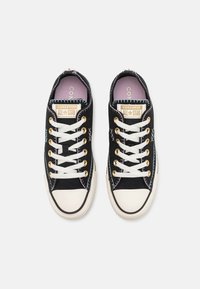 Baskets en toile noires avec des embouts en caoutchouc blanc. Présentent des œillets dorés, des lacets blancs et une semelle intérieure rose. Marque Converse All-Star sur l'étiquette.