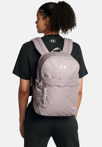 Mochila de color rosa claro con correas de hombro acolchadas, un bolsillo frontal con cremallera y acento de logo. Fabricada con un tejido suave y duradero de textura lisa.