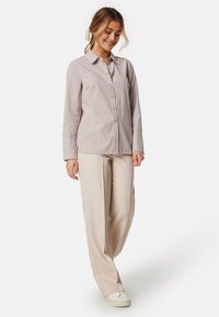 Camicia a maniche lunghe, con bottoni, color beige chiaro con sottili righe verticali. Abbinata a pantaloni larghi color crema e sneaker casual.