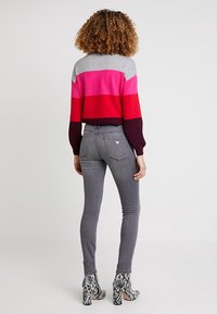 Suéter de punto con rayas horizontales en gris, rosa, rojo y burdeos; combinado con vaqueros ajustados grises y botines de tacón con estampado de serpiente.
