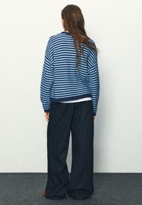 Modrý a námornícky pruhovaný pletený sveter s voľným strihom, kombinovaný so širokými tmavými rifľovými nohavicami. Viditeľné textúrované materiály.