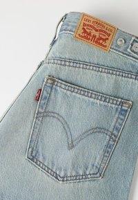 Ανοιχτό μπλε denim τζιν Levi's που δείχνουν την πίσω τσέπη, την κόκκινη ετικέτα Levi's και το δερμάτινο κεντητό με την εικόνα δύο αλόγων.