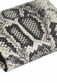 Portefeuille en imitation serpent noir et blanc avec une surface texturée, présentant une forme rectangulaire élégante et des accents en métal argenté.