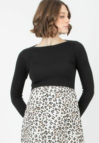 Schwarzes, geripptes Langarmoberteil kombiniert mit einem weißen Kleid, das am Saum ein schwarz-orangefarbenes Leopardenmuster aufweist.
