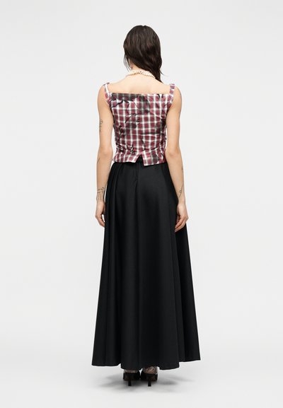 Punavalkoruudullinen istuva paita, jossa kukkakuvioita, yhdistetty pitkään mustaan hameeseen. Takana paljas selkä ja helma lievästi liehuva.