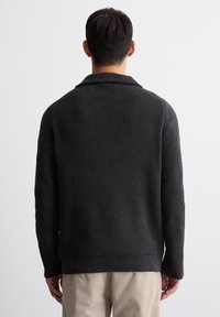 Dunkelgrauer, gerippter Strickpullover mit weitem Kragen, langen Ärmeln und lockerem Sitz. Die Textur ist weich und leicht dehnbar.