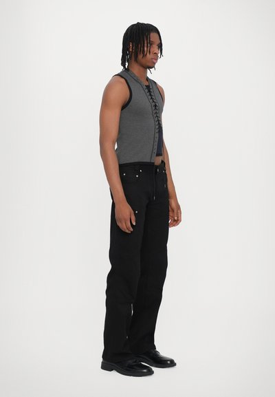 Haut en tricot gris sans manches avec un design à lacets à l'avant. Associé à un pantalon noir à jambe droite et des chaussures noires. Un style simple et moderne.