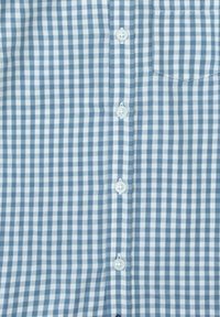 Camisa de cuadros en azul y blanco con frente de botones, pequeño bolsillo y textura suave. Los botones son redondos y blancos.