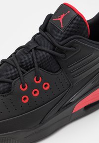 Černá sportovní bota s prodyšnou síťovinou a koženými materiály, červenými akcenty, šesti otvory pro šněrování, výrazným šněrováním a logem na jazyku.