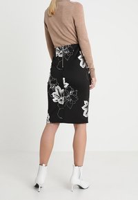 Černá květinová tužková sukně s bílými květinovými vzory, vyrobená z elastického materiálu. Kombinována s bílými kotníkovými botami a béžovým svetr.