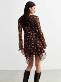 Abito floreale nero con maniche lunghe in pizzo trasparente, orlo asimmetrico e intricati motivi di fiori rosa. Abbinato a stivali neri lucidi al ginocchio.