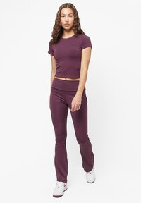 Burgunderfarget tettsittende kort topp med korte ermer, matched med høyt liv leggings, laget av elastisk stoff, brukt sammen med hvite joggesko.