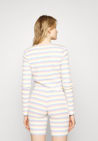 Conjunto de roupa de lazer às riscas em cores pastel de rosa, azul, amarelo e branco. O tecido é suave, de ajuste justo, com mangas longas e calções.