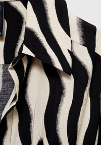Tissu rayé noir et blanc avec un motif audacieux et irrégulier formant une partie d’un vêtement à col.
