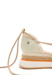 Sneaker en toile beige et suède avec une semelle intermédiaire en jute tressé, détail d'accent orange et lacets rayés marron. Présente un logo en métal argenté.