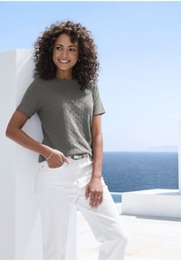 Grauer, strukturierter Kurzarm-Top, kombiniert mit weißen Hosen und einem sichtbaren silbernen Gürtelakzent; Ozean und Himmel im Hintergrund.