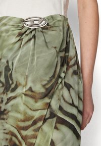 Fustă verde din chiffon cu un model în dungi de tigru, prezentând o cataramă ovală argintie la talie și detalii subtile de drapare.