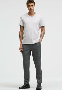 Weißes V-Ausschnitt-T-Shirt aus leichtem Stoff, kombiniert mit grauen karierten Hosen und schwarzen Stiefeletten. Minimalistisches Design, kurze Ärmel.