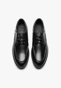 Chaussures en cuir noir avec une finition lisse, un design à lacets, des orteils arrondis et des coutures contrastantes le long des bords. Semelles intérieures légèrement rembourrées.