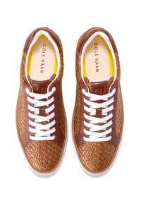 Braune gewobene Sneaker mit Lederakzenten, weißen Schnürsenkeln und einem gelben Innenfutter. Die Sohle hat eine helle sandfarbene Farbe und eine strukturierte Griffigkeit.