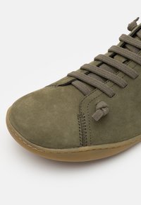 Scarpa in suede verde oliva con punta arrotondata, suola piatta in gomma beige e dettagli con lacci annodati. Presenta cuciture verticali lungo il lato.
