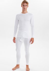 Hvid langærmet top med rund halsudskæring og tætsiddende hvide termolegins. Begge dele er lavet af et blødt, strækbart stof.