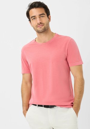 Kurzärmliges T-Shirt mit Rundhalsausschnitt aus pastellrosa Baumwolle. Glatte Textur, lockere Passform und dezente Stichdetails. Trägt man mit hellen Hosen.