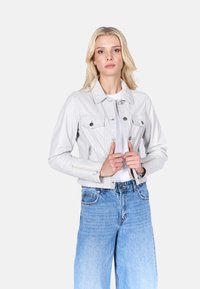 Witte denim jas met twee borstzakken, ritsdetails en knopen. Gecombineerd met blauwe wijde jeans en een eenvoudig wit T-shirt.