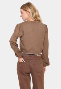 Brun kortärmad tröja med puffärmar, ribbade ärmmuddar och en texturerad yta, kombinerad med bruna höga byxor med bakfickor.