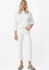 Top de punto blanco de manga larga combinado con jeans rectos de tiro alto en blanco roto. El conjunto presenta un corte relajado y un diseño minimalista.